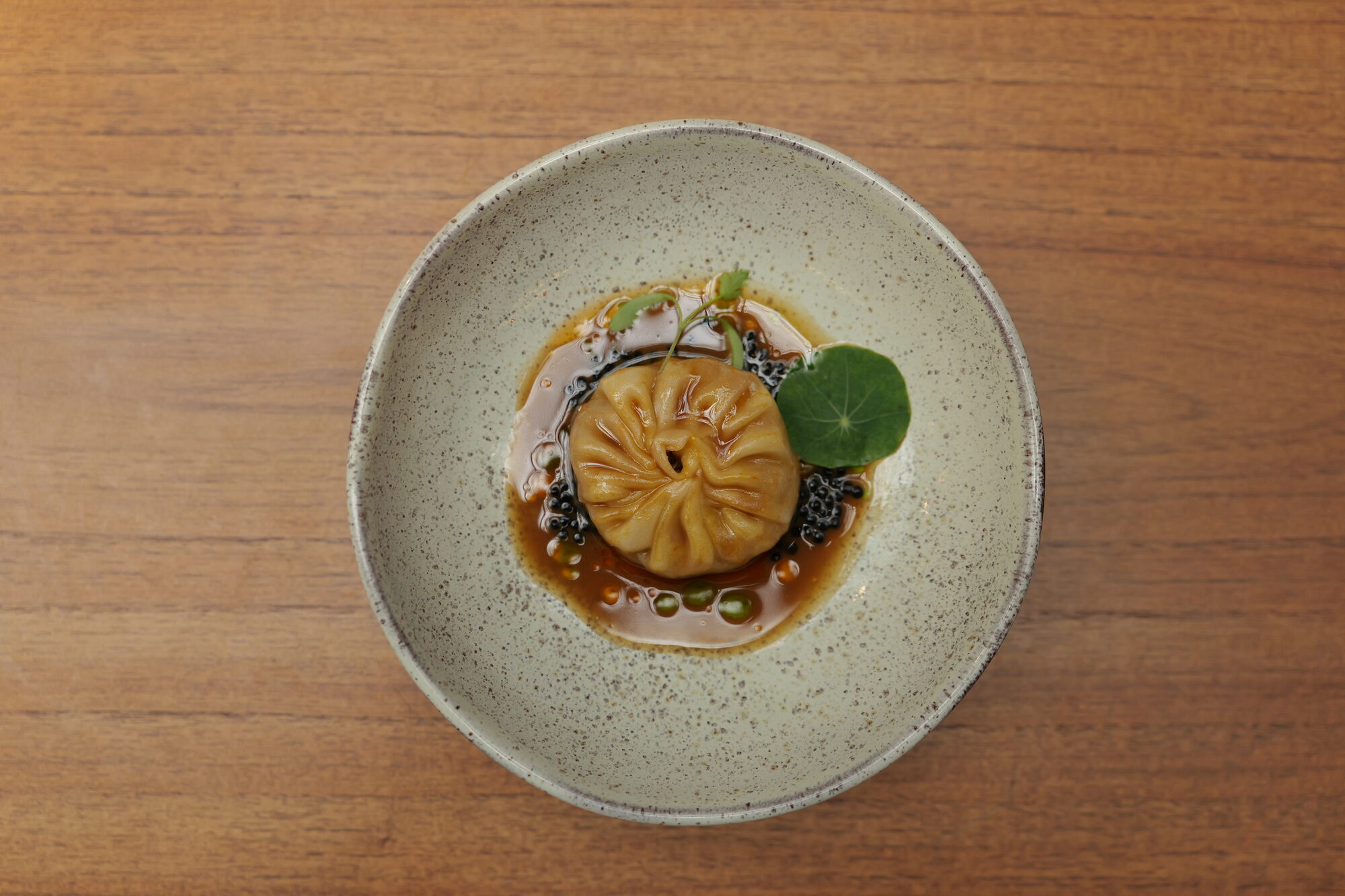 Dumpling em caldo escuro com ovas e folha de capuchinha