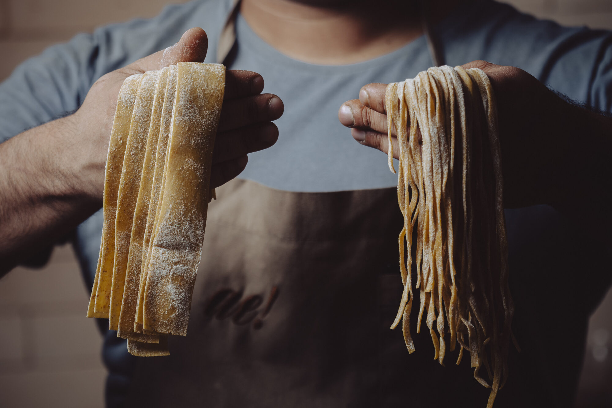 Cozinheiro segurando pappardelle e linguine frescos, feitos na casa